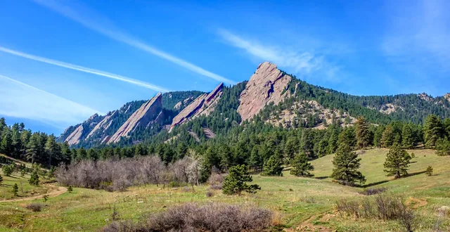 Angled rock formations rise above green foothills beneath a bright blue sky.