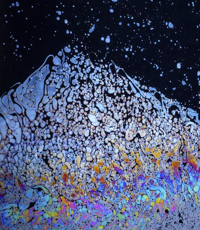 A dark surface covered in bright bubbles and patches of iridescent color.