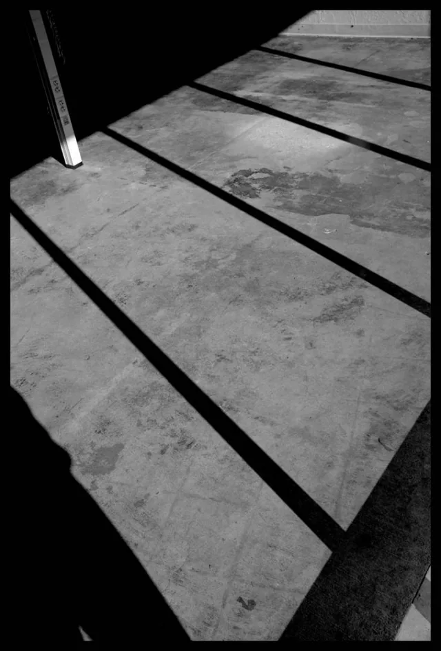 Diagonal bands of sunlight and shadow cross concrete in a black-and-white composition.