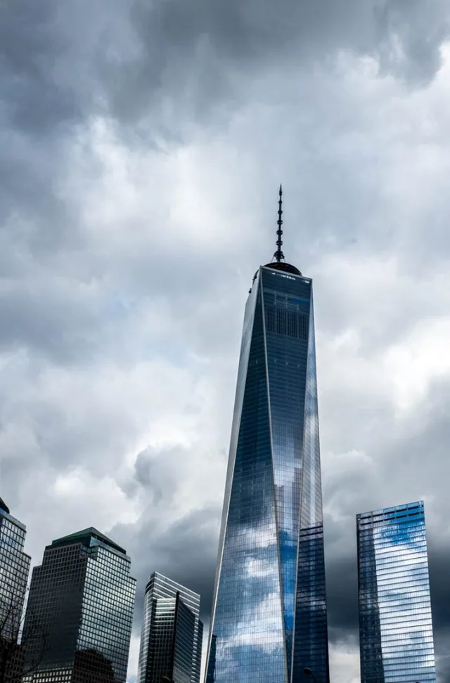 A tall glass skyscraper rises into a cloudy sky.