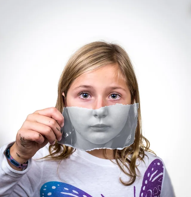 A child holds a monochrome portrait over the lower half of their face.