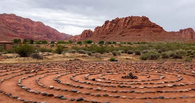 A spiral of stones on red earth with desert cliffs in the background.