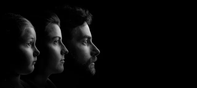 Three faces in profile emerge from darkness in a black-and-white portrait.