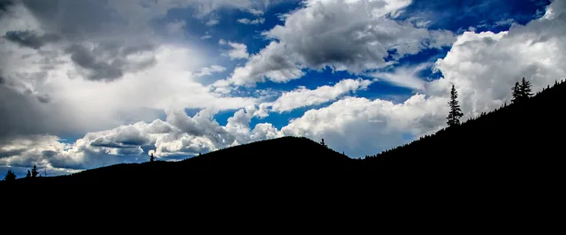 Dramatic white and gray clouds rise above a dark mountain silhouette.
