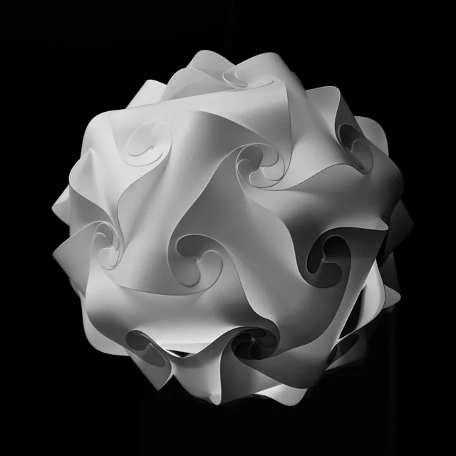 A white spherical sculpture made of curled, folded forms against black.