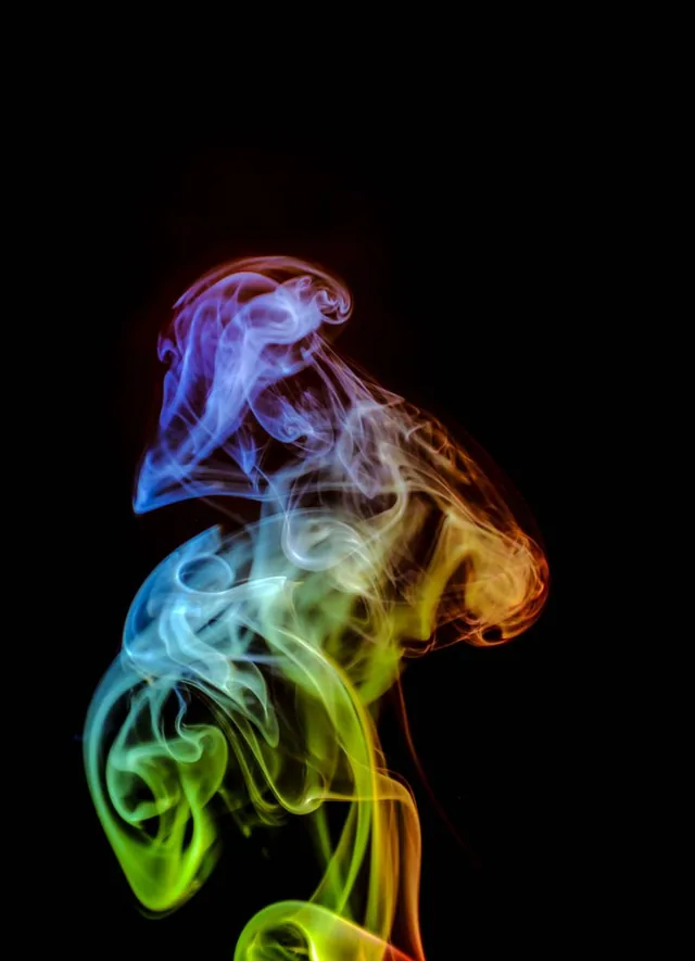 A vertical plume of multicolored smoke twists against a black background.